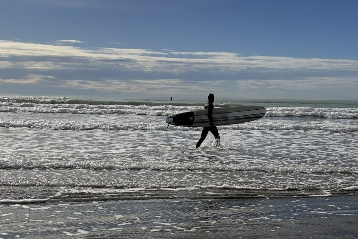 Surfer entering water at beach in Sumner New Zealand