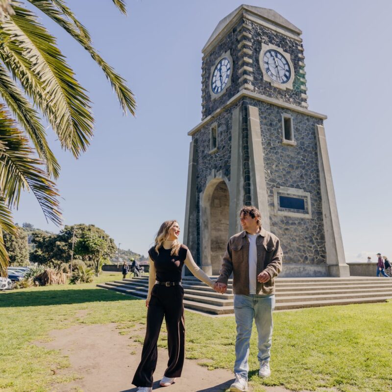 Couple walking beneath SUmner clock tower during their stay at affordable Christchurch motel near Sumner village
